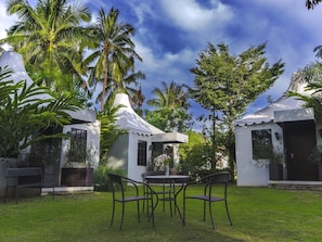 A tropical outdoor area with a dining table and chairs, surrounded by palm trees and a white building.