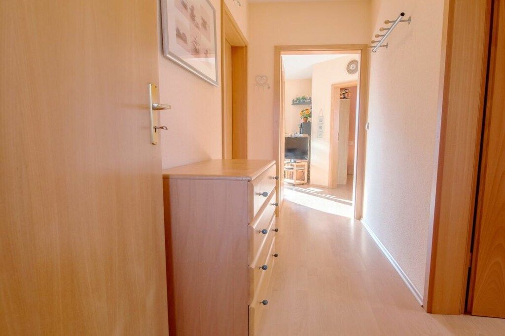 Un pasillo con un armario de madera, una puerta con perchero y una vista parcial de una habitación con televisor y planta.