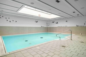 An indoor swimming pool with a tiled floor, a handrail, and wall murals of birds and reeds. - 3.5/T3 holiday home park “Freesenbruch” (Zingst (Ostseeheilbad))