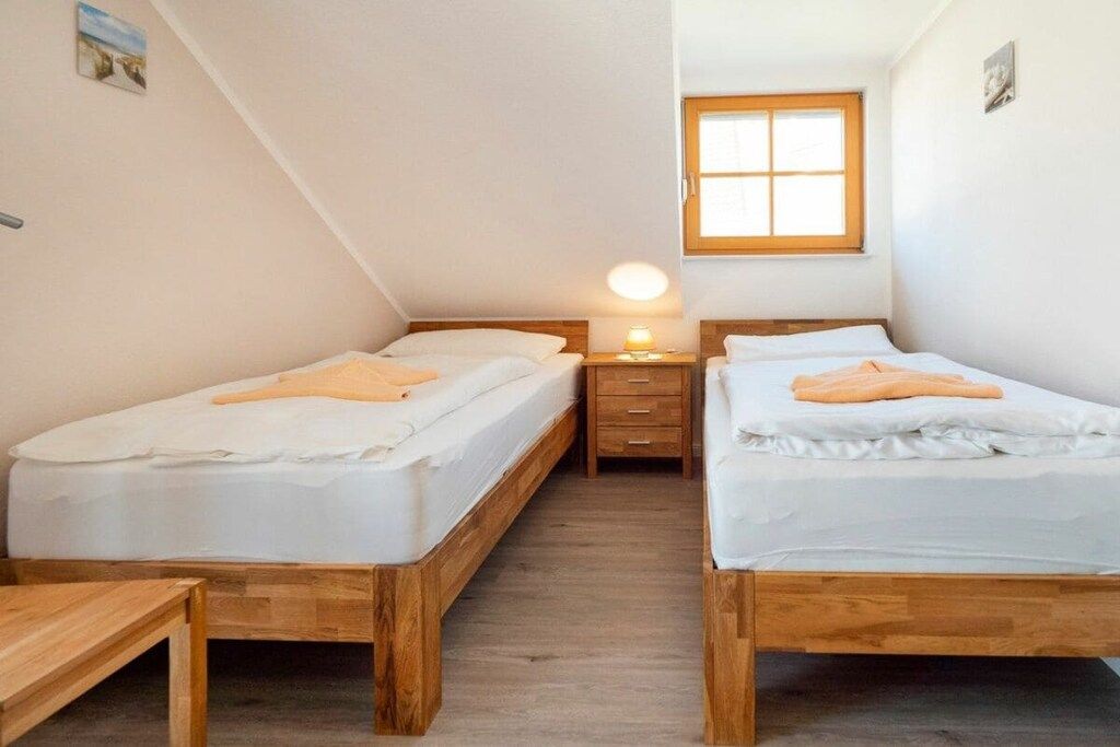 Une petite pièce agréable, dotée de deux lits en bois, d’une table de chevet avec une lampe et d’une fenêtre.