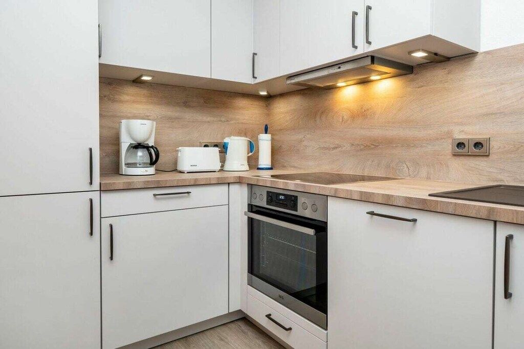A modern kitchen with white cabinets, a built-in oven, a coffee maker, and a toaster.