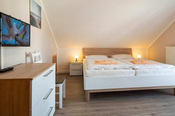 A bedroom with a bed, bedside tables, a desk, and a television mounted on the wall. - 6b/T5 Holiday Park "Freesenbruch" (Zingst (Ostseeheilbad))