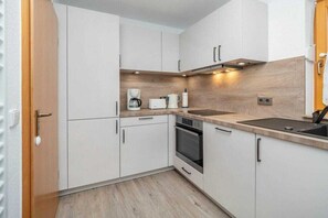A compact kitchen with white cabinets, a wooden countertop, a built-in oven, and a coffee maker. - 6b/T5 Holiday Park "Freesenbruch" (Zingst (Ostseeheilbad))