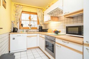 A compact kitchen with a dishwasher, oven, microwave, and a window with curtains. - 2.1/T2 holiday home park “Freesenbruch” (Zingst (Ostseeheilbad))
