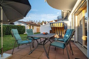 An outdoor patio with a table and chairs, a striped umbrella, and a view of a residential area. - 2.1/T2 holiday home park “Freesenbruch” (Zingst (Ostseeheilbad))
