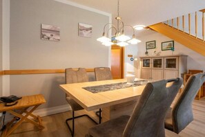A dining area with a wooden table, grey upholstered chairs, a small side table with a phone, and a staircase in the background. - 8a/T5 Holiday Park "Freesenbruch" (Zingst (Ostseeheilbad))