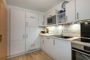 A modern kitchen with white cabinetry, a microwave, a sink, and an oven. - 8a/T5 Holiday Park "Freesenbruch" (Zingst (Ostseeheilbad))
