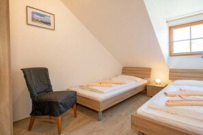 Une petite pièce agréable, dotée de deux lits en bois, d’une chaise et d’une table de chevet avec une lampe.