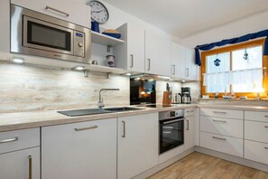 A modern kitchen with white cabinetry, a built-in oven, a microwave, and a sink. - 8a/T5 Holiday Park "Freesenbruch" (Zingst (Ostseeheilbad))