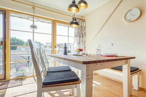 Een eetruimte met een houten tafel, twee stoelen en een bank. Er is een raam met uitzicht op gebouwen.