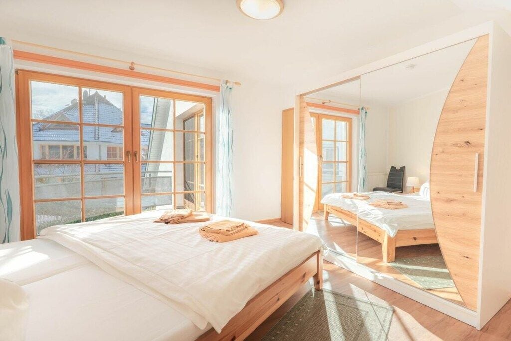 A bedroom with a large mirror, wooden bed frames, and a view of a house through the window.