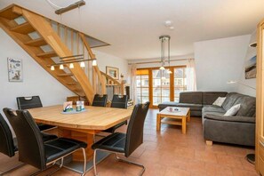 Ein stilvoller Wohnraum mit einer Holztreppe, einem Essbereich mit Holztisch und -stühlen, einem Sofa und einem Couchtisch.