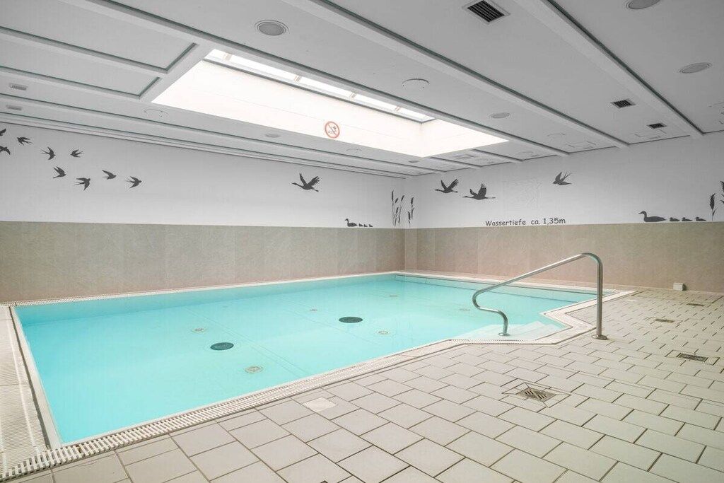 Una piscina con suelo de baldosas, baranda y murales de aves.
