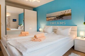 A bedroom with a large bed, two side tables, a mirror, and a wall with the word 'DREAMS' above it. - 3.2/T4 holiday home park “Freesenbruch” (Zingst (Ostseeheilbad))