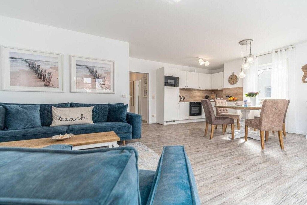 Un salon moderne avec un canapé bleu, un coin repas avec une table et des chaises, et une cuisine en arrière-plan.