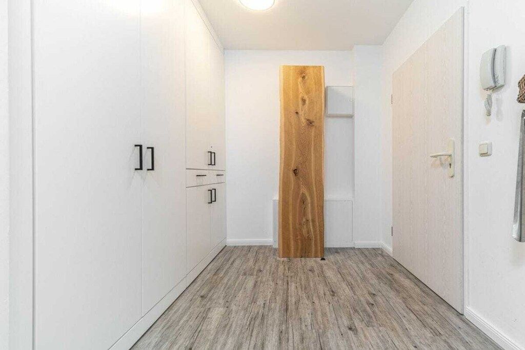 Ein schmaler Flur mit weißen Wänden, einer Holztür und einem weißen Kleiderschrank mit zwei Schubladen.