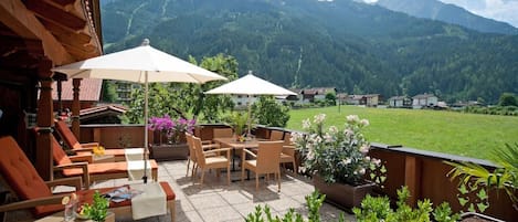Un patio al aire libre con mesa y sillas, rodeado de macetas con plantas y vistas a un paisaje montañoso.
