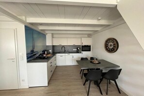 Eine moderne Küche mit weißen Schränken, einem Esstisch mit Stühlen und einer Uhr an der Wand.