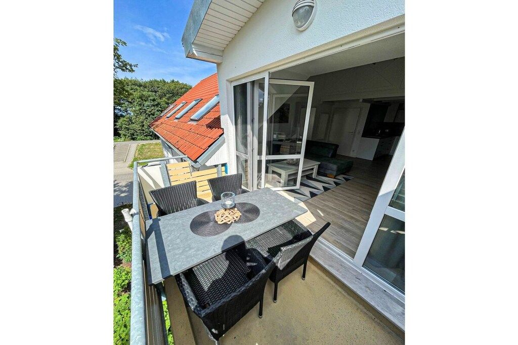 An outdoor patio with a table and chairs, a sliding glass door leading to a living area, and a red-roofed building in the background.