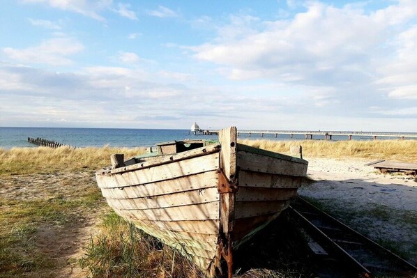Un bote de madera en una playa arenosa con un muelle al fondo.
