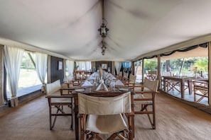 A tented dining area with tables set for a meal, featuring a central hanging light fixture. - Serengeti Pioneer Camp (Bariadi)