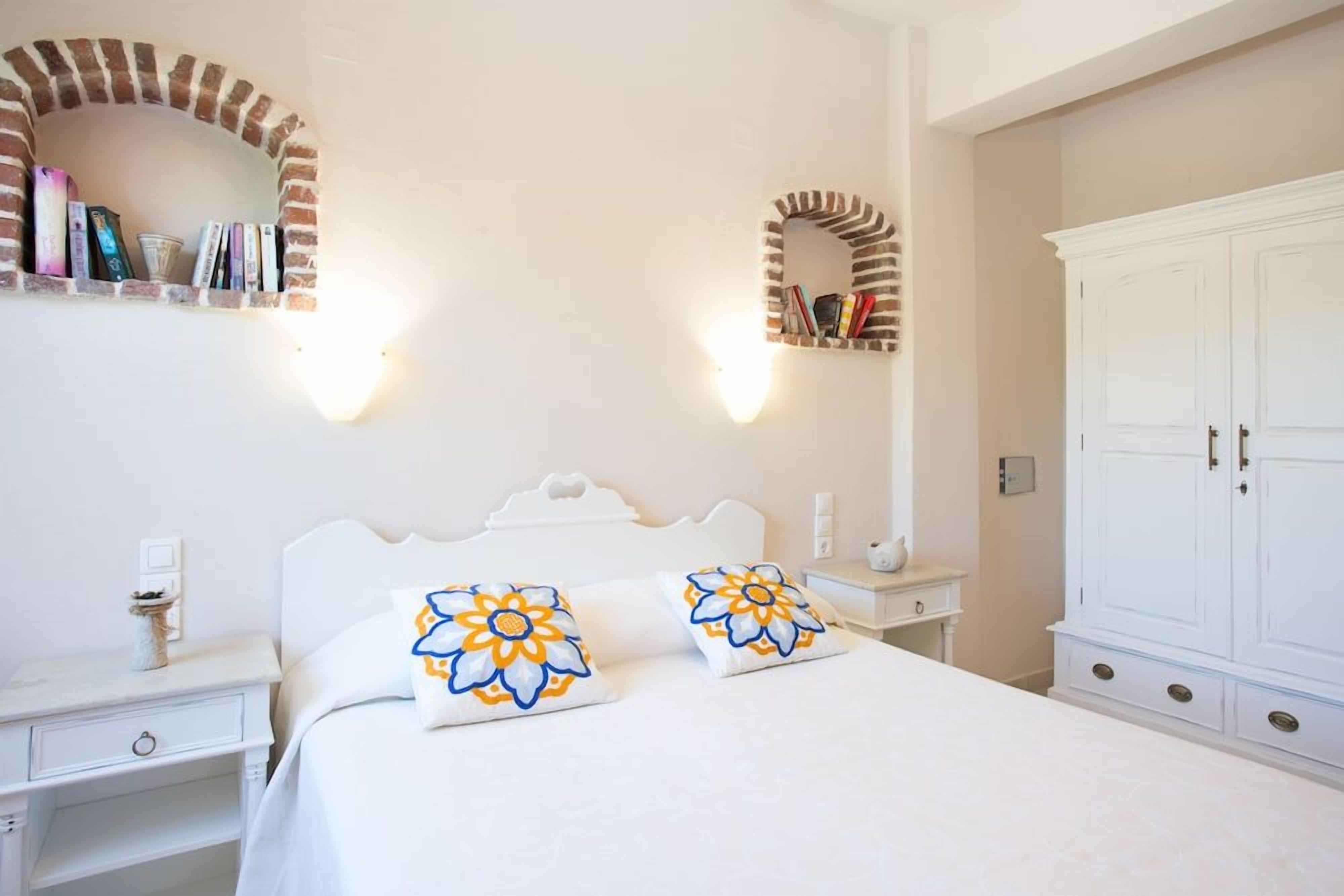 A bedroom with a bed, two nightstands, a wardrobe, and two wall-mounted shelves with books.