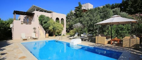 A swimming pool with lounge chairs and a pergola, surrounded by a stone patio and lush greenery.