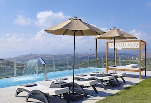 Zona junto a la piscina con sillones de descanso, sombrillas y una cascada.