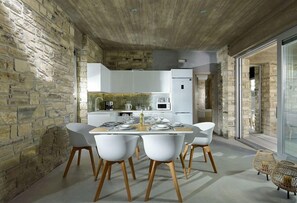 A modern kitchen with white cabinets, a dining table set for four, and a stone wall.