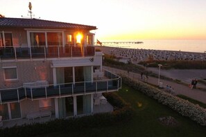 Ein zweistöckiges Gebäude mit einem Balkon, der auf einen Strand und einen Pier im Hintergrund blickt.