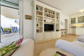 Una sala de estar con televisión, estanterías, comedor y vistas al exterior.