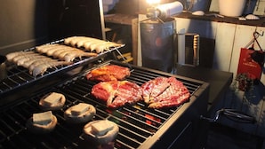 A grill with various meats and mushrooms being cooked. - Okinawan. Sweet Home.t-8 (Chatan)