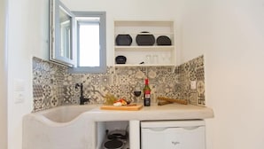 A compact kitchen with a built-in stove, a small refrigerator, and a window above the sink. - Ampelos Inn (Naxos)