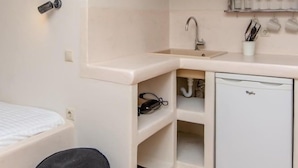 A compact kitchen with a built-in sink, a small refrigerator, and a shelf with dishes. - Ampelos Inn (Naxos)