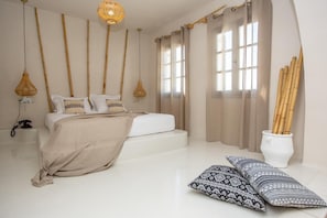 Quarto com cama, luminárias de cabeceira, telefone e um vaso com galhos de bambu.