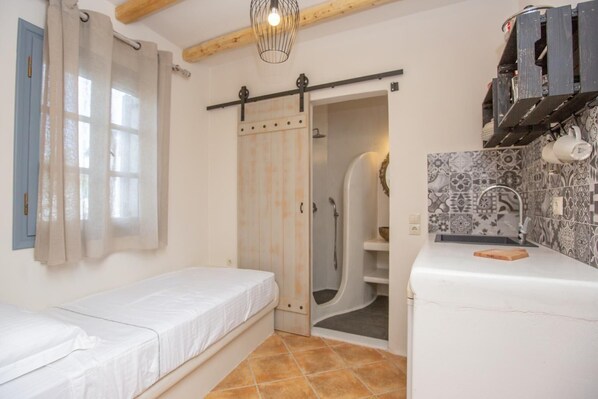 A compact room with a bed, a shower area, and a kitchenette. - Ampelos Inn (Naxos)