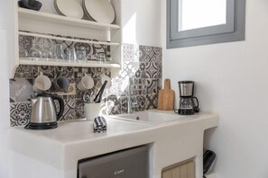 Cozinha com bancadas brancas, cafeteira, chaleira e escorredor de louça.