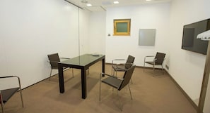 Un salón de conferencias con una mesa de vidrio, cuatro sillas, una pizarra y un televisor en la pared.