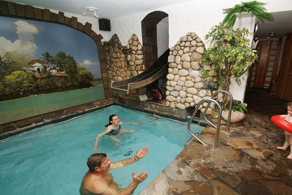 An indoor swimming pool with a slide, stone walls, and a mural of a tropical scene.