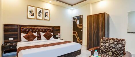 A hotel room with a bed, a wardrobe, a sofa, a coffee table with items, and framed artwork on the wall.