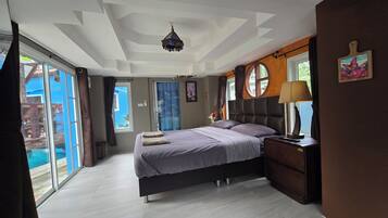 A bedroom with a bed, bedside table, lamp, and a view of the outdoors.