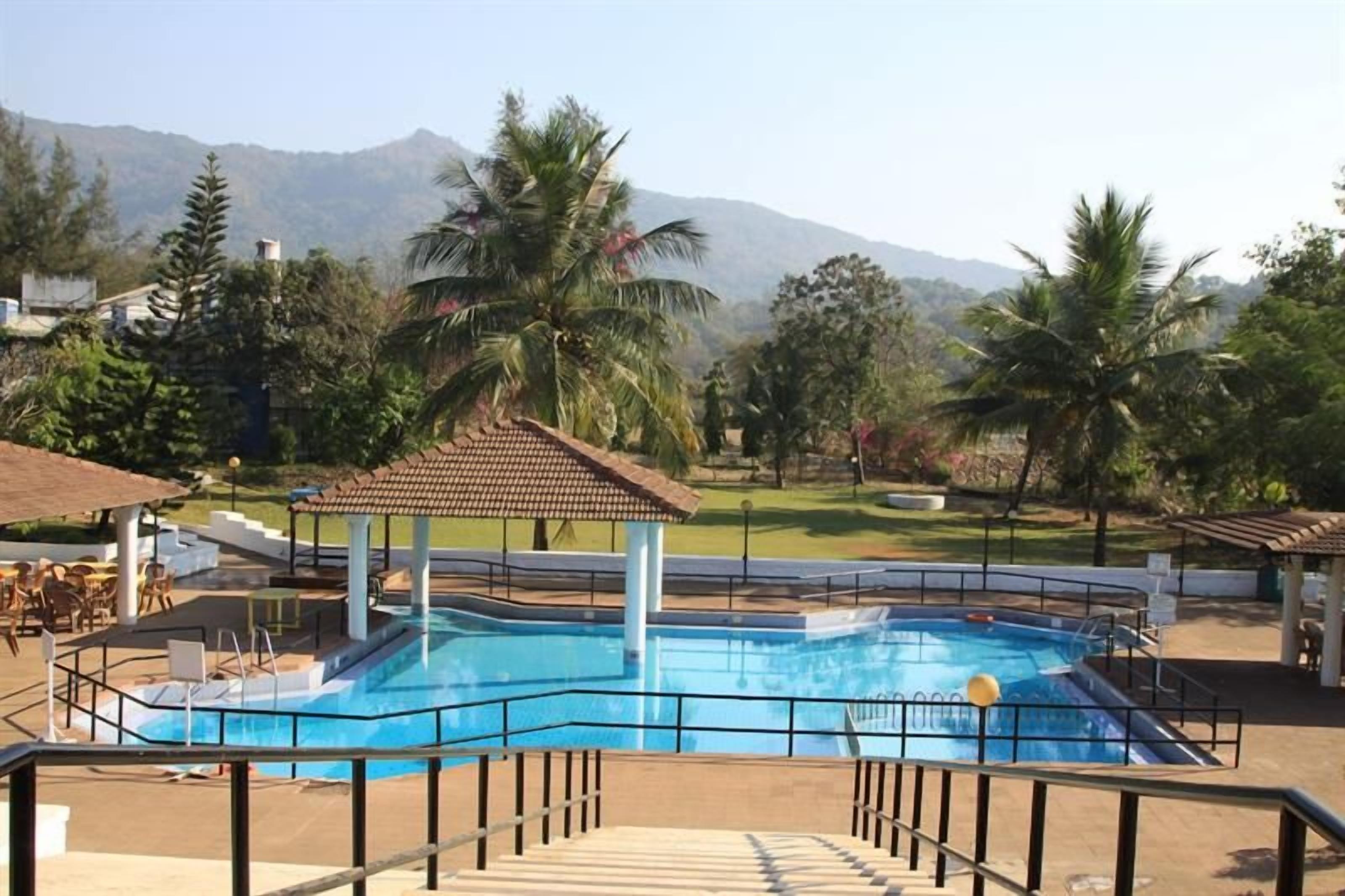 A swimming pool with a gazebo, surrounded by palm trees and a mountain backdrop.