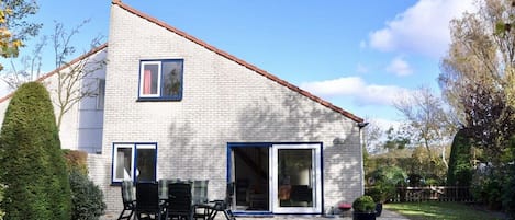 A two-story house with a brick exterior, a small window, and a sliding glass door leading to a patio with outdoor furniture.