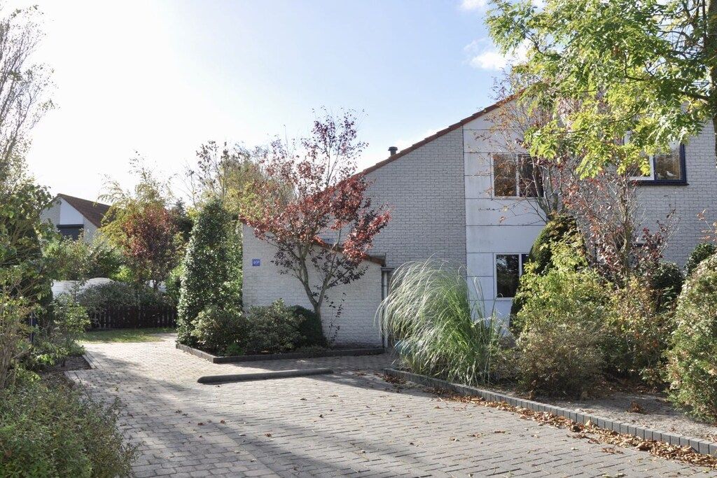 Un edificio residencial con entrada pavimentada, rodeado de arbustos y árboles.