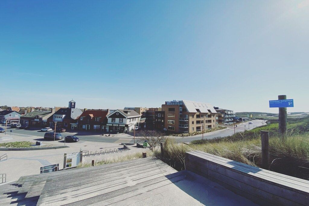 A coastal town with a mix of residential and commercial buildings, a clear sky, and a road leading into the distance.