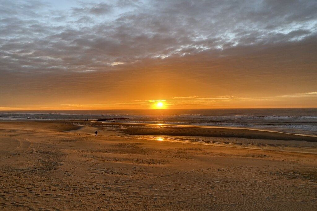 Une plage au coucher du soleil, avec du sable et quelques personnes qui se promènent.