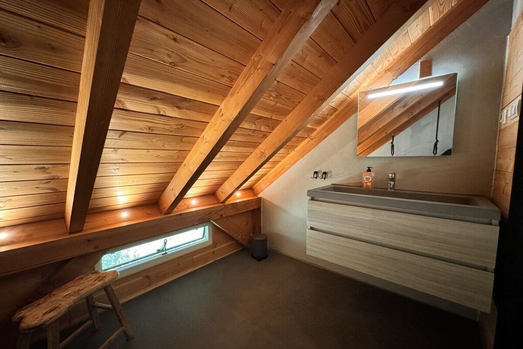 Een badkamer met een houten plafond, een raam en een wastafel met spiegel.