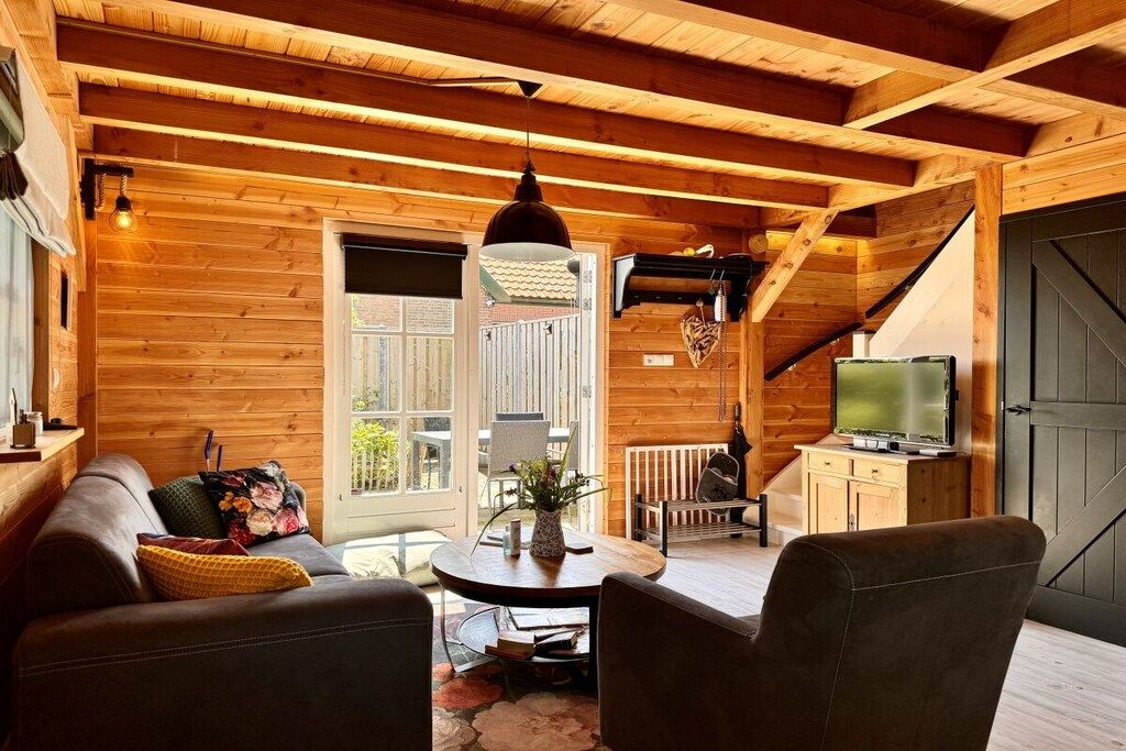 En mysig stuga med träpanel i taket, en soffa, ett bord med en vas och en tv.