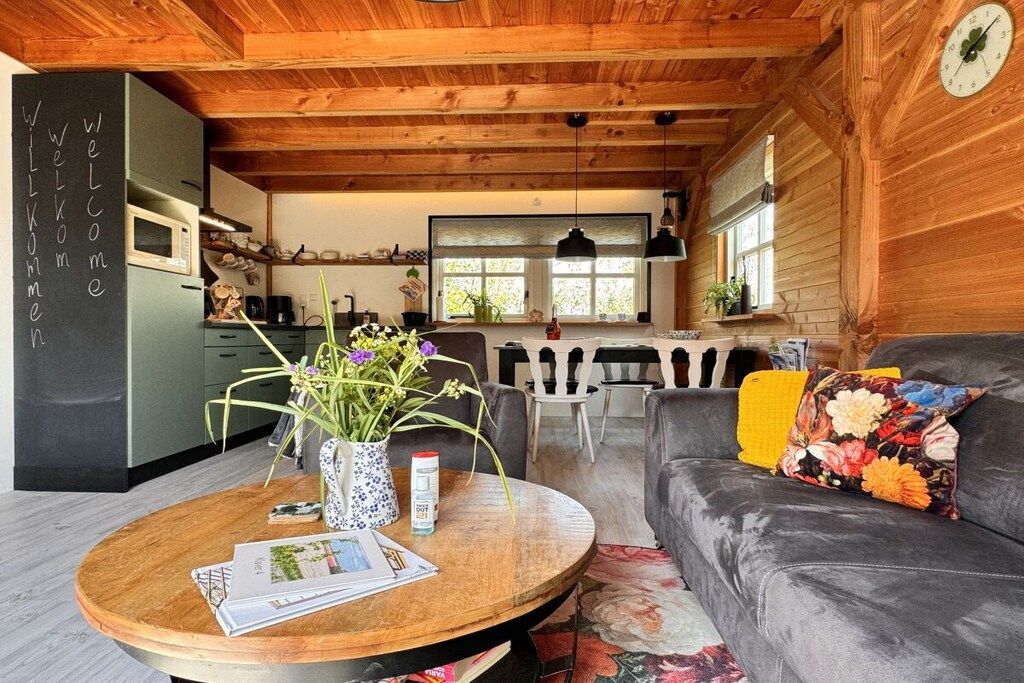 Ein gemütliches Interieur mit Holzbalkendecke, einem Essbereich mit Tisch und Stühlen, einer Couch mit floralen Kissen und einer Küche mit modernen Geräten.