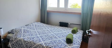 Una habitación de hotel con cama, ventana con cortinas, radiador y puerta.